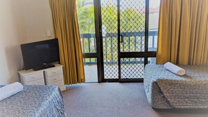 Habitación de hotel con dos camas, un televisor en una cómoda y una puerta corrediza de vidrio al exterior.