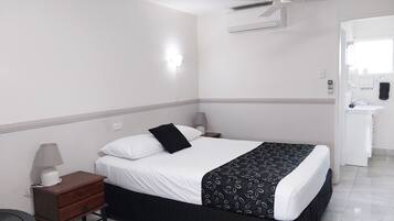A hotel room with a bed, bedside tables, a lamp, an air conditioning unit, and a bathroom with a sink and mirror.