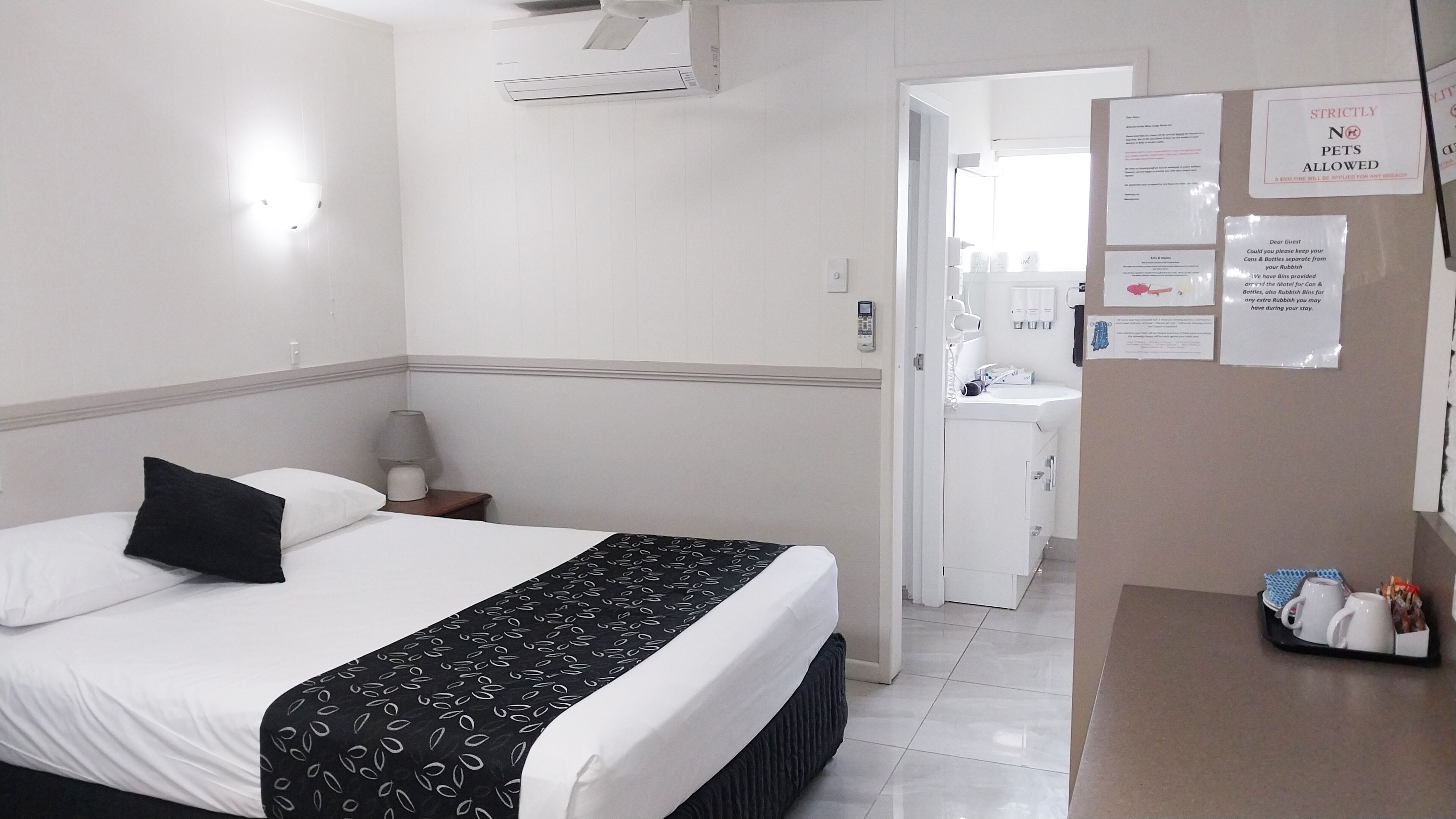 Hotelkamer met een bed, nachtkastje, bureau met lamp, spiegel en een zichtbare badkamer door een geopende deur.