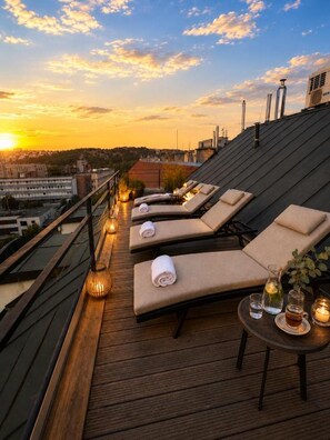 Eine Dachterrasse mit Liegestühlen, einem Holzboden und Blick auf den Sonnenuntergang.