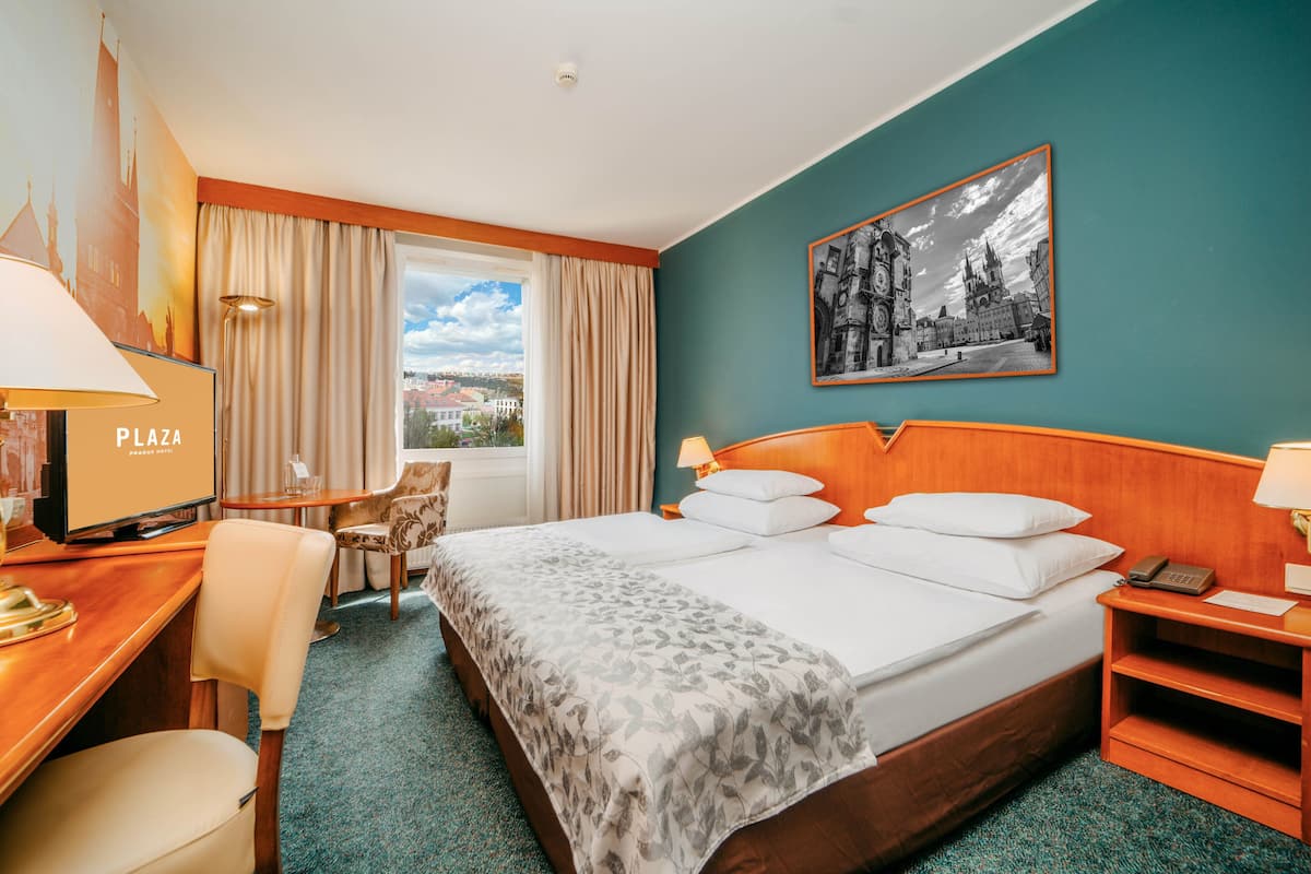 Habitación de hotel con cama, escritorio, silla, televisor y ventana con cortinas.