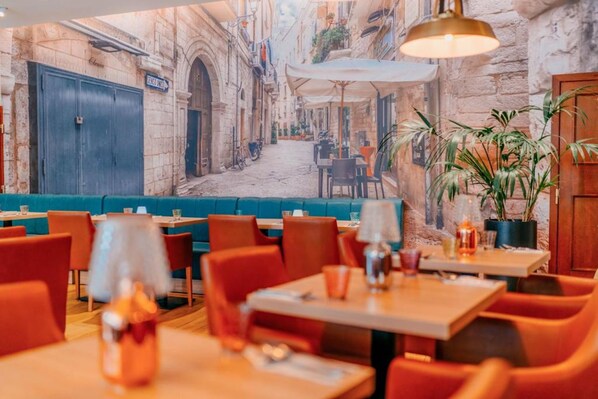 Un restaurant amb un mural d'una escena de carrer, taules i cadires de fusta i una làmpada penjant.
