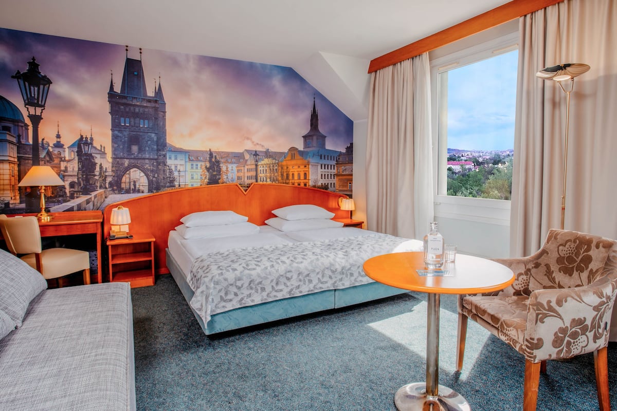 Habitación de hotel con una cama grande, un escritorio, una silla, una mesita y vistas a un paisaje urbano a través de la ventana.