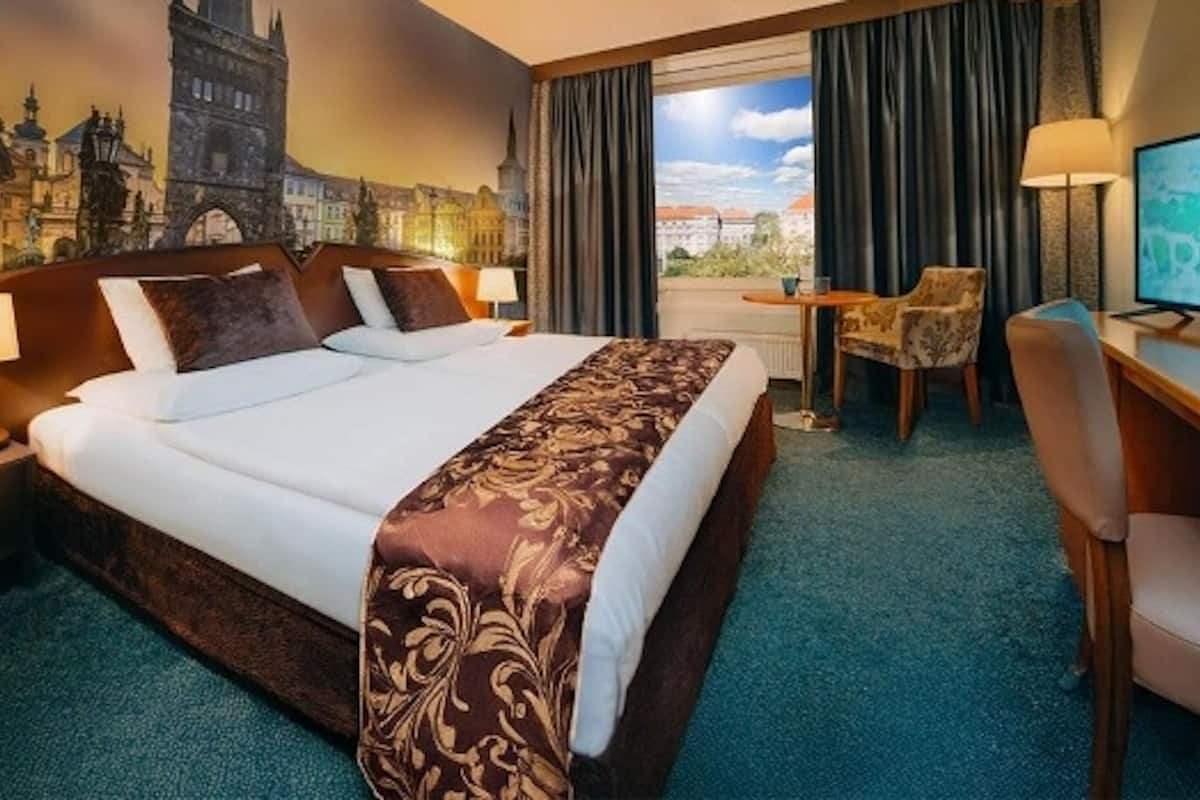Una habitación de hotel con una cama grande, un escritorio con una silla, un televisor y un mural con una vista urbana en la pared.