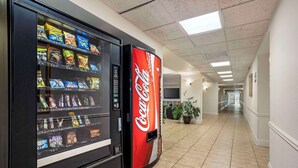 A vending machine and a Coca-Cola refrigerator in a hallway with tiled flooring and a ceiling with fluorescent lights. - Quality Inn & Suites NRG Park - Medical Center (Houston)