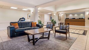 A lobby with a black leather sofa, wooden coffee table, and two upholstered chairs. A reception desk is visible in the background. - Quality Inn & Suites NRG Park - Medical Center (Houston)