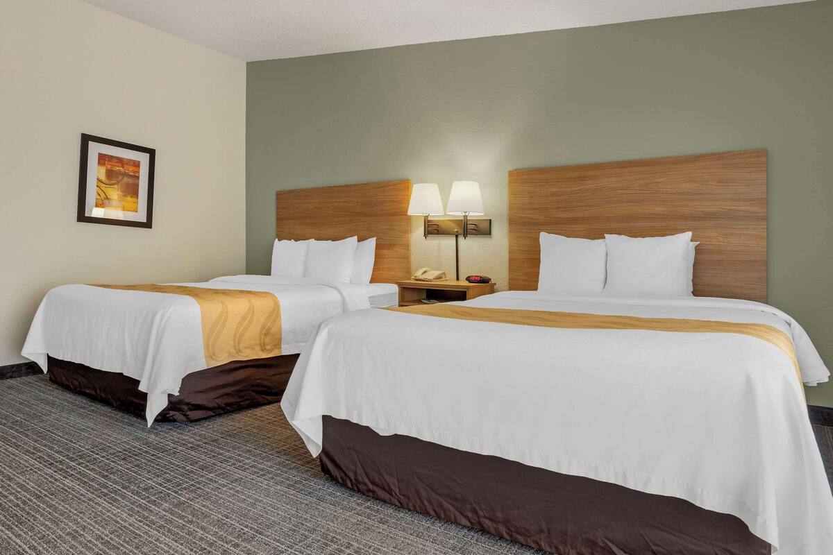A hotel room with two beds, a nightstand with lamps, and a framed picture on the wall.