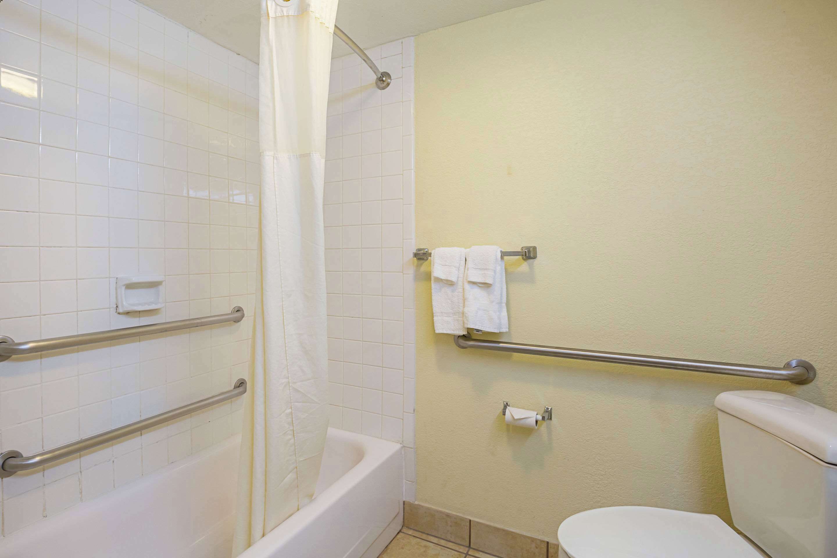 A bathroom with white tiles, a bathtub, a toilet, and a shower curtain.