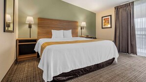 A hotel room with a large bed, two bedside tables, a nightstand, a mirror, and a window with curtains. - Quality Inn & Suites NRG Park - Medical Center (Houston)