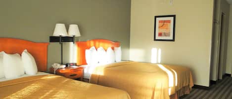A hotel room with two beds, a nightstand with a lamp, a framed picture on the wall, and a carpeted floor.