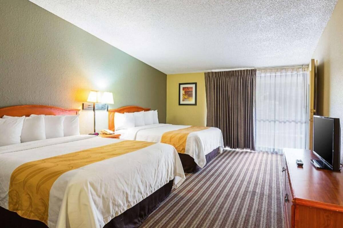 A hotel room with two beds, a television, a lamp, and a window with curtains.