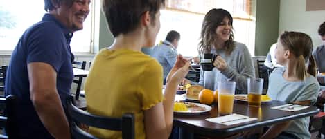 Un comedor con mesas y sillas, una ventana con persianas y vistas al exterior.