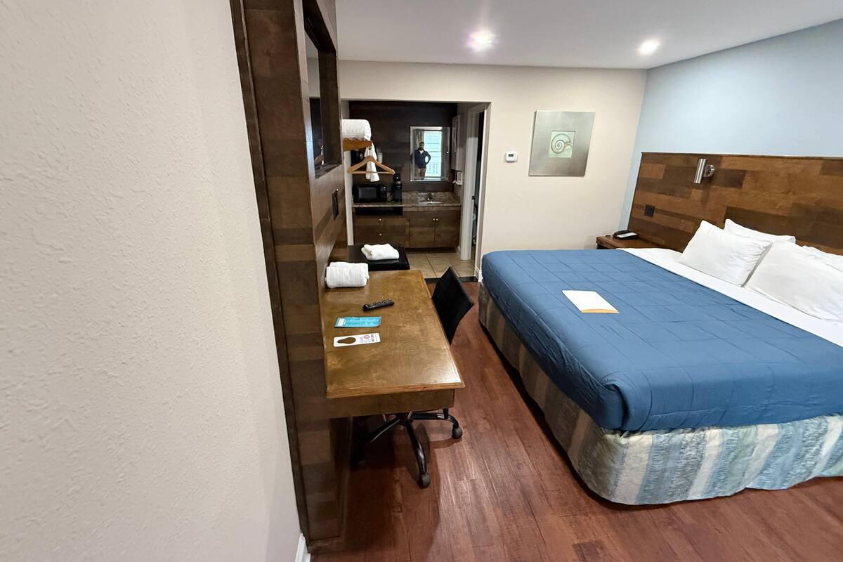 A hotel room with a wooden desk, a bed with a blue bedspread, a nightstand, and a mirror.