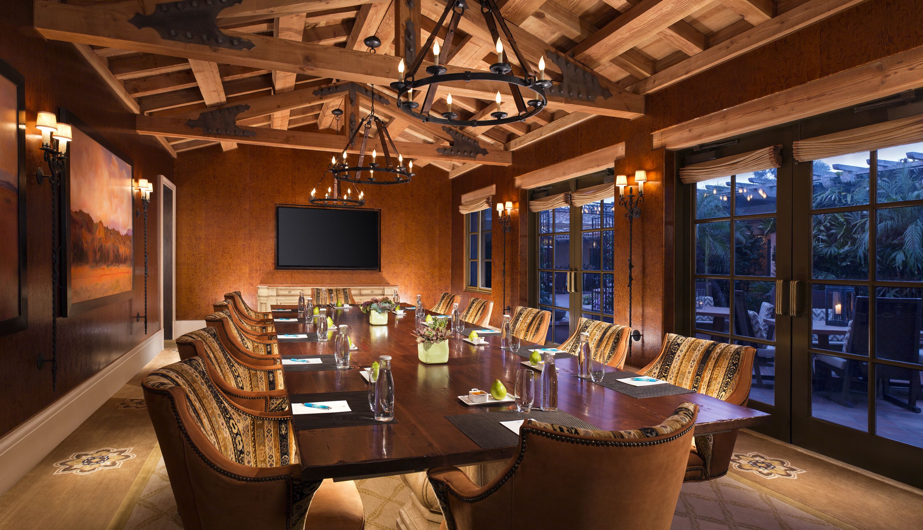 A conference room with a long table, chairs, and a chandelier. There is a large window with a view of the outdoors.
