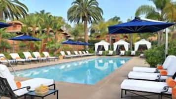 A pool area with lounge chairs and umbrellas, surrounded by palm trees and a clear sky.