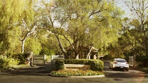 A gated entrance with a stone sign, a white car parked inside, and a well-maintained garden with red flowers. - Rancho Valencia Resort and Spa (Rancho Santa Fe)