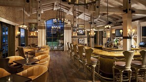 A bar area with leather seating, a bar counter, and a large window overlooking a view. - Rancho Valencia Resort and Spa (Rancho Santa Fe)
