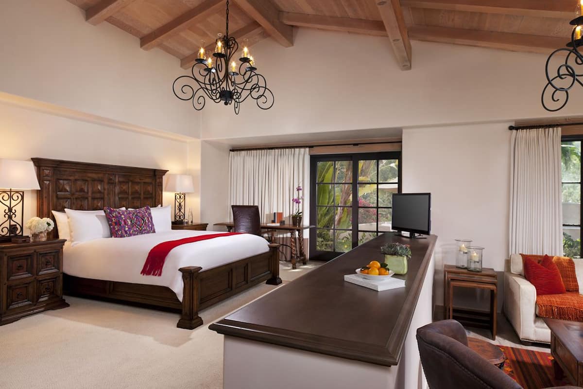 A bedroom with a large bed, wooden headboard, bedside tables, a TV, a desk, and a sofa.