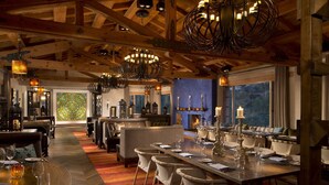 A spacious dining area with a long table set for multiple guests, a fireplace, and a view of the outdoors. - Rancho Valencia Resort and Spa (Rancho Santa Fe)