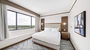 Une chambre d’hôtel avec un grand lit, une vue sur la ville, une tête de lit en bois et une table de chevet avec une lampe.