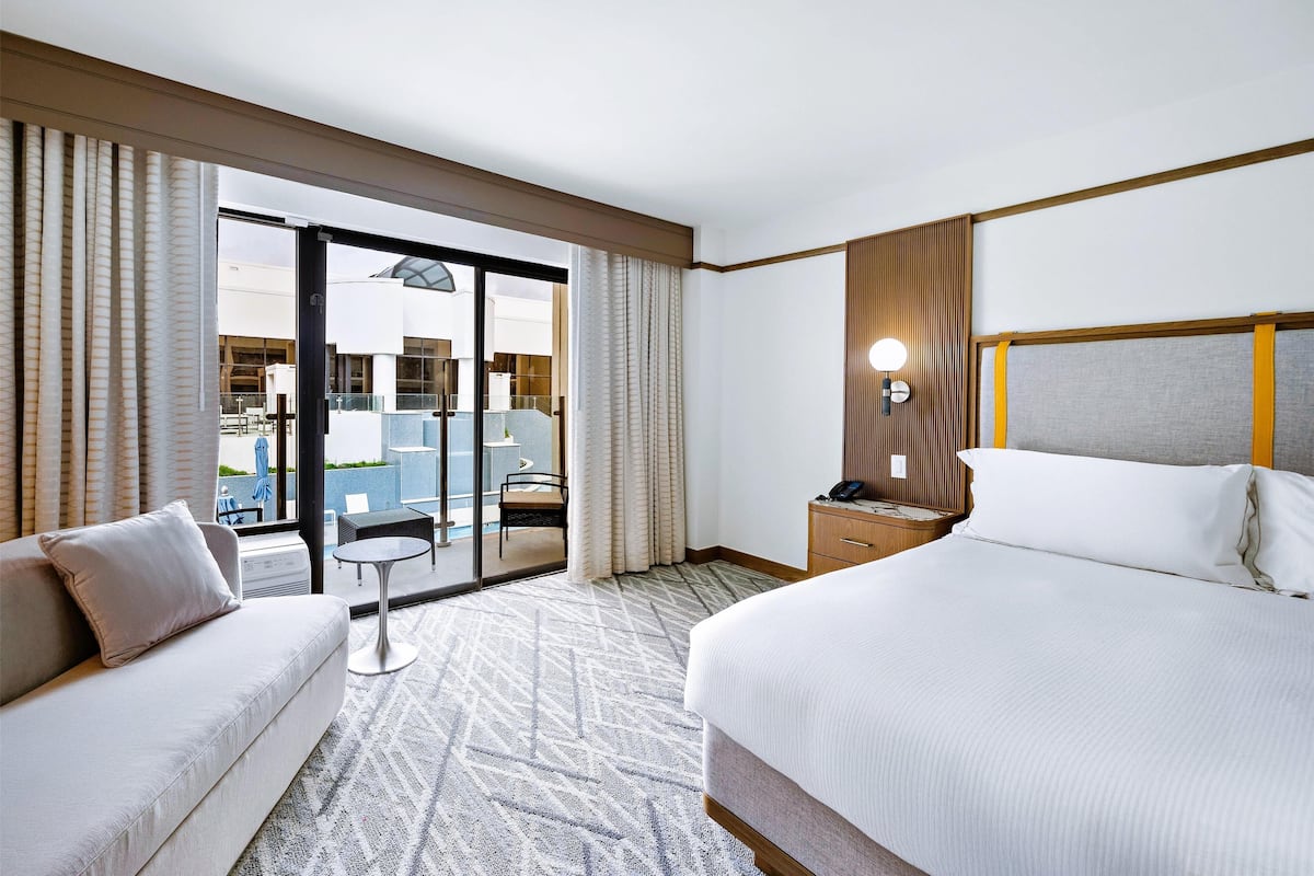 A hotel room with a large bed, a sofa, a small table, and a balcony with a view of the outside.