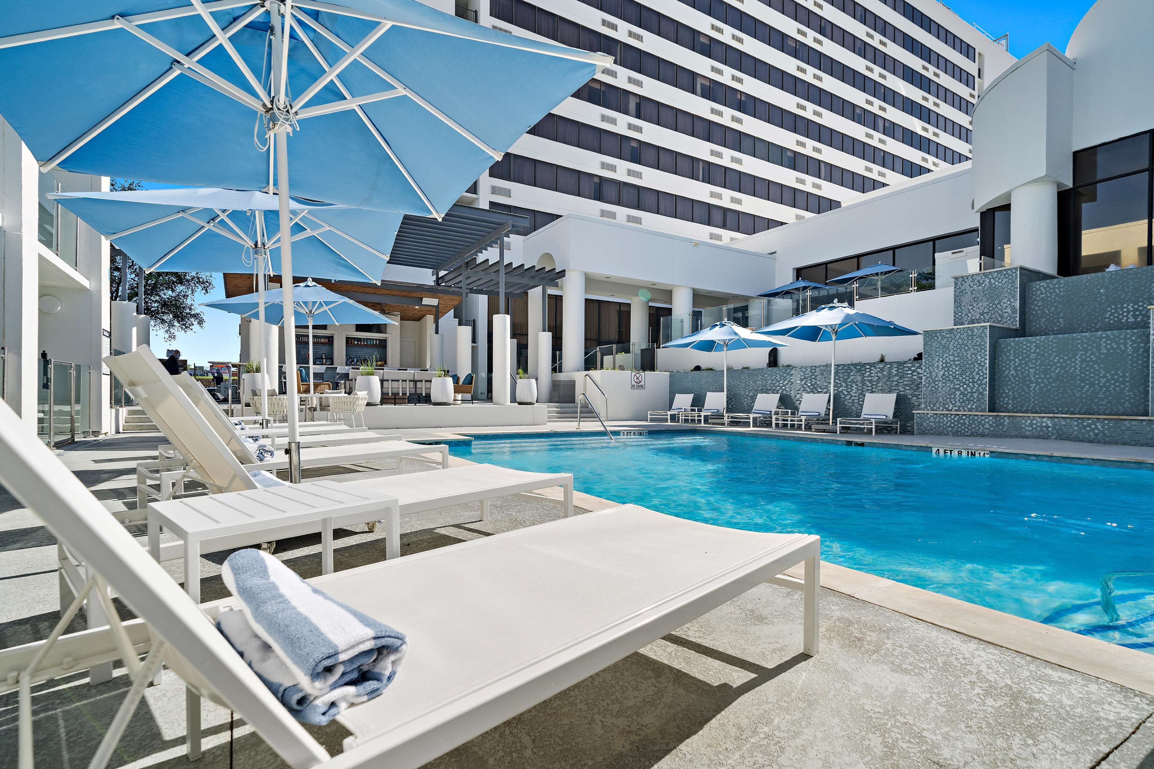 Una piscina al aire libre, sombrillas, sillones reclinables de piscina