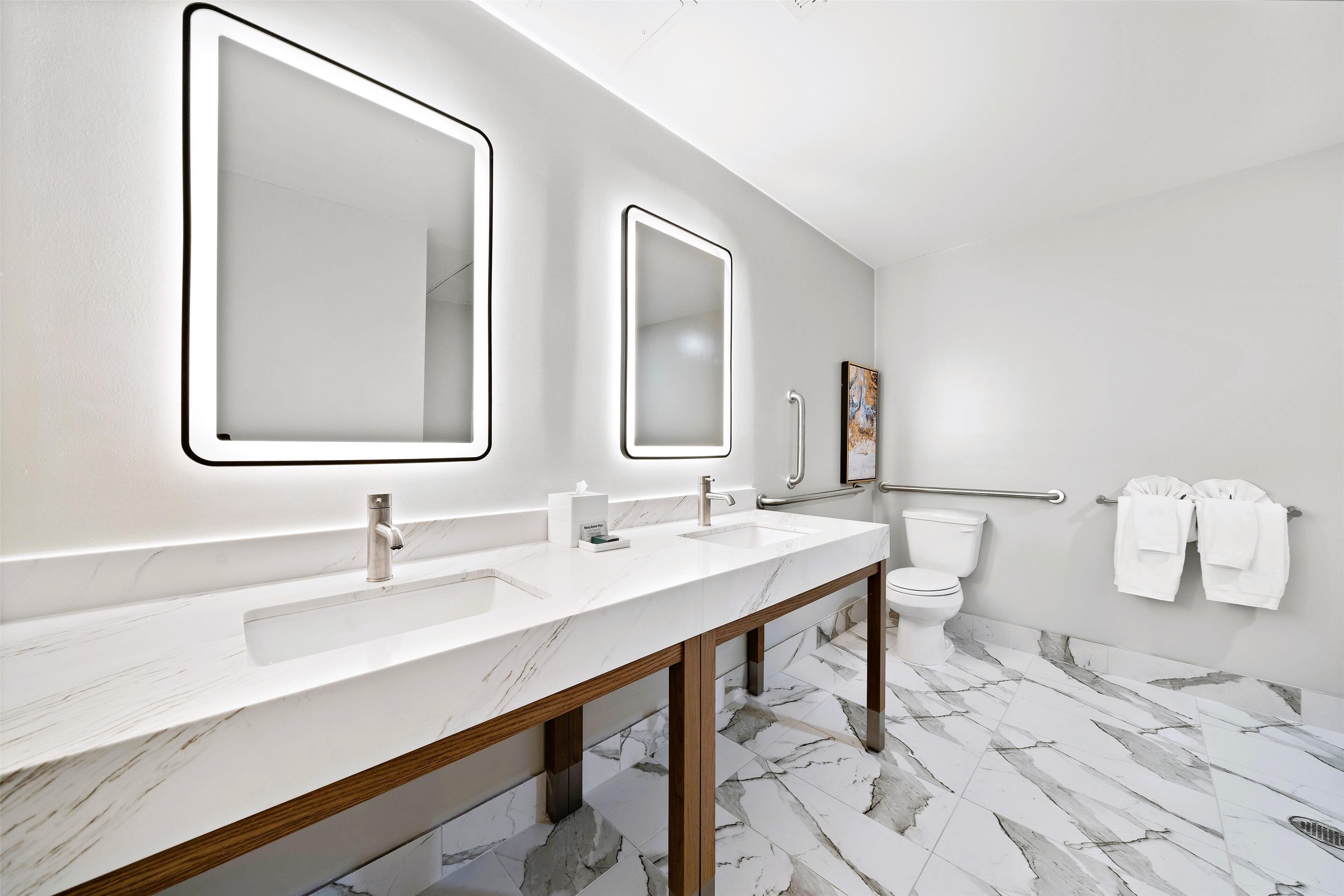 A modern bathroom with two sinks, a toilet, and a handrail.