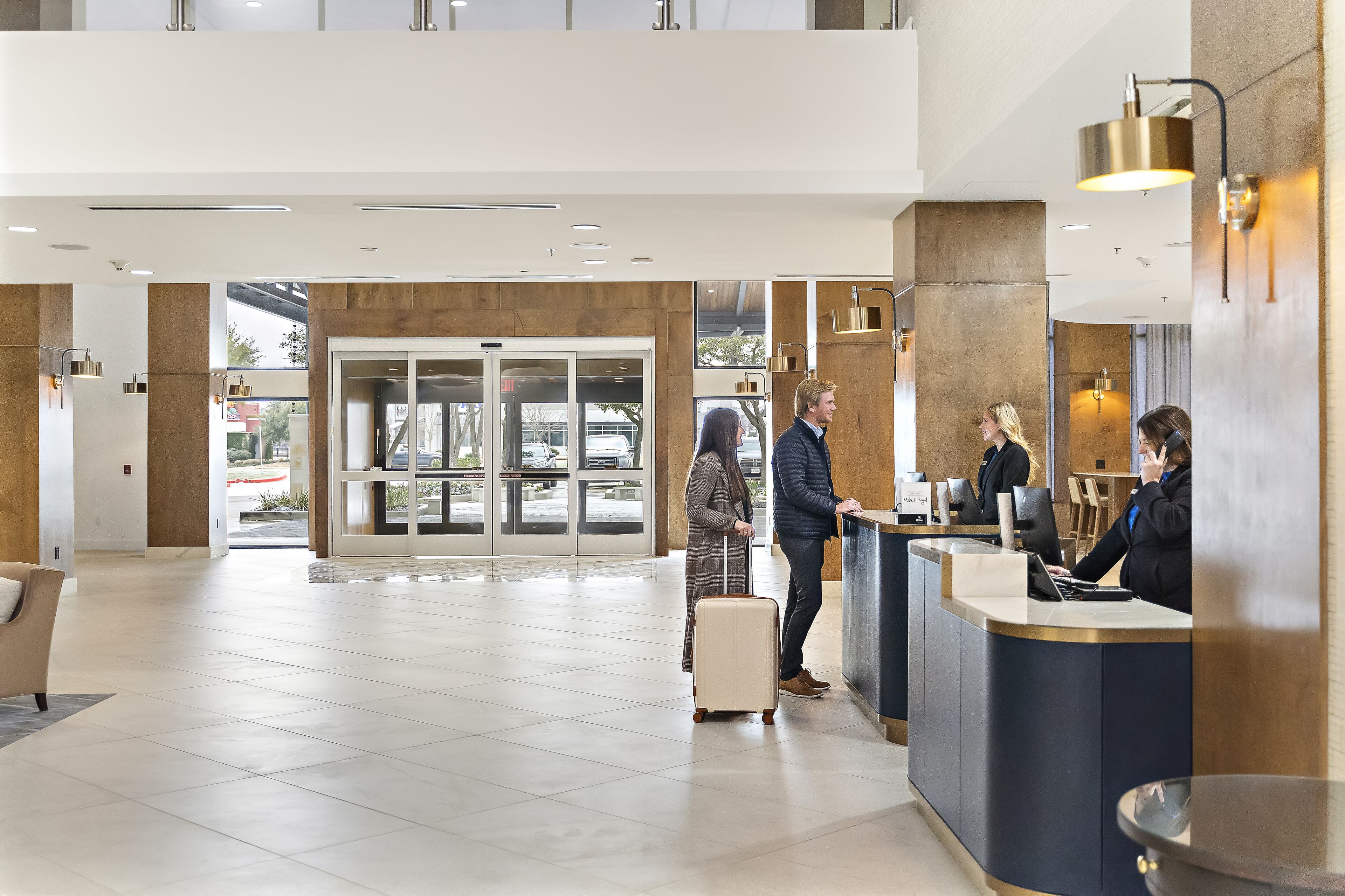 A modern reception area with a check-in counter, a waiting area with a sofa, and a view through the glass doors to the outside.