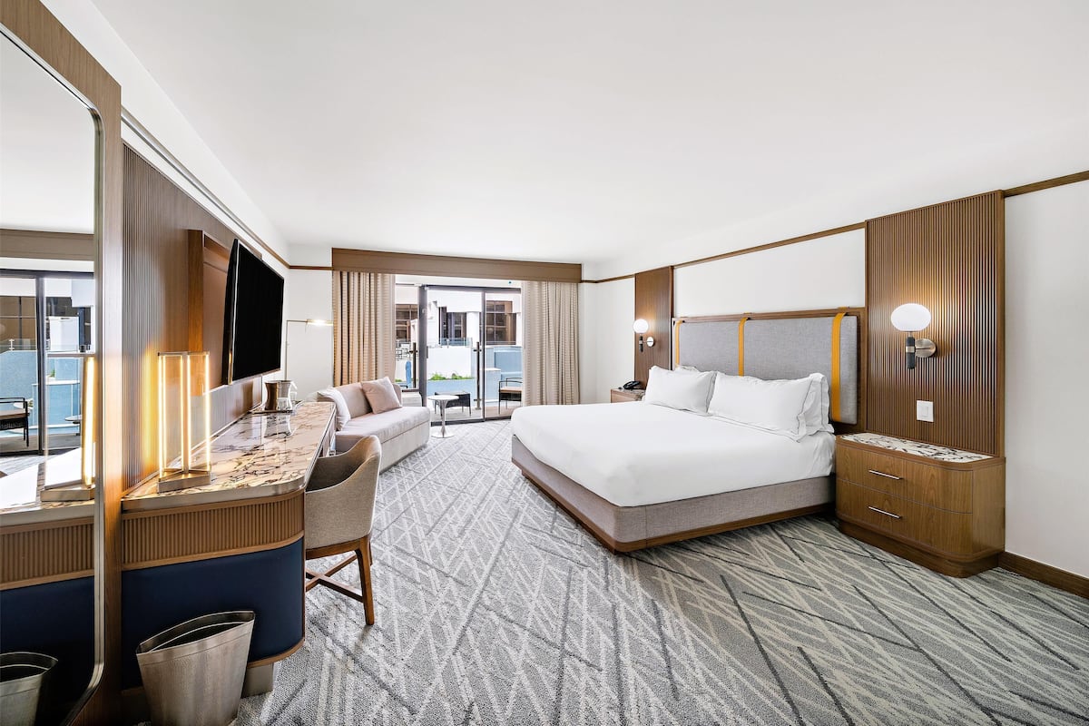 A hotel room with a bed, desk, and chair, a large window, and a view of the outside.