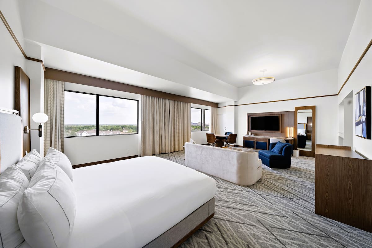 A hotel room with a large bed, a sofa, a desk, and a TV.