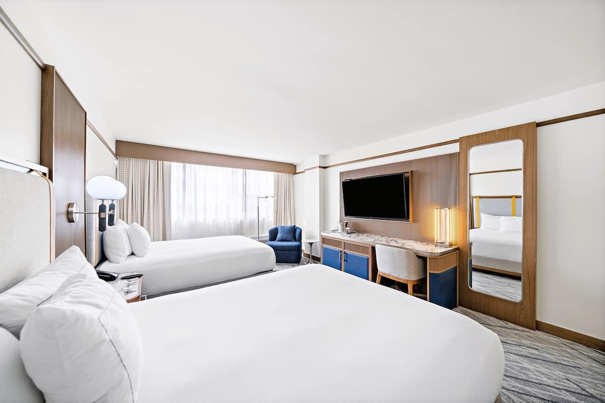 A hotel room with two beds, a desk with a chair, a TV, and a large mirror.