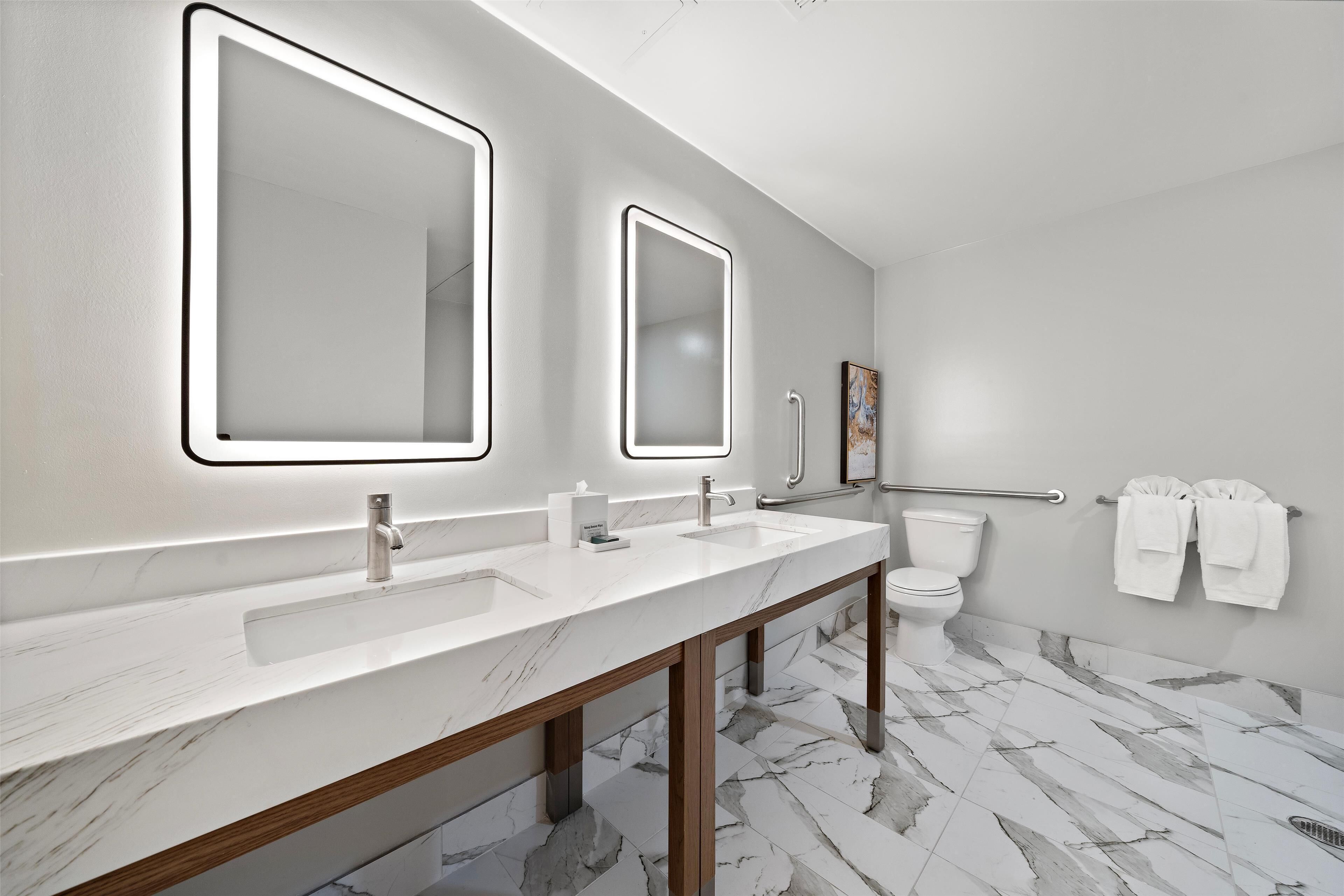 A modern bathroom with two sinks, a toilet, and a handrail.