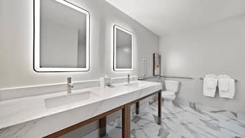 A modern bathroom with two sinks, a toilet, and a handrail.