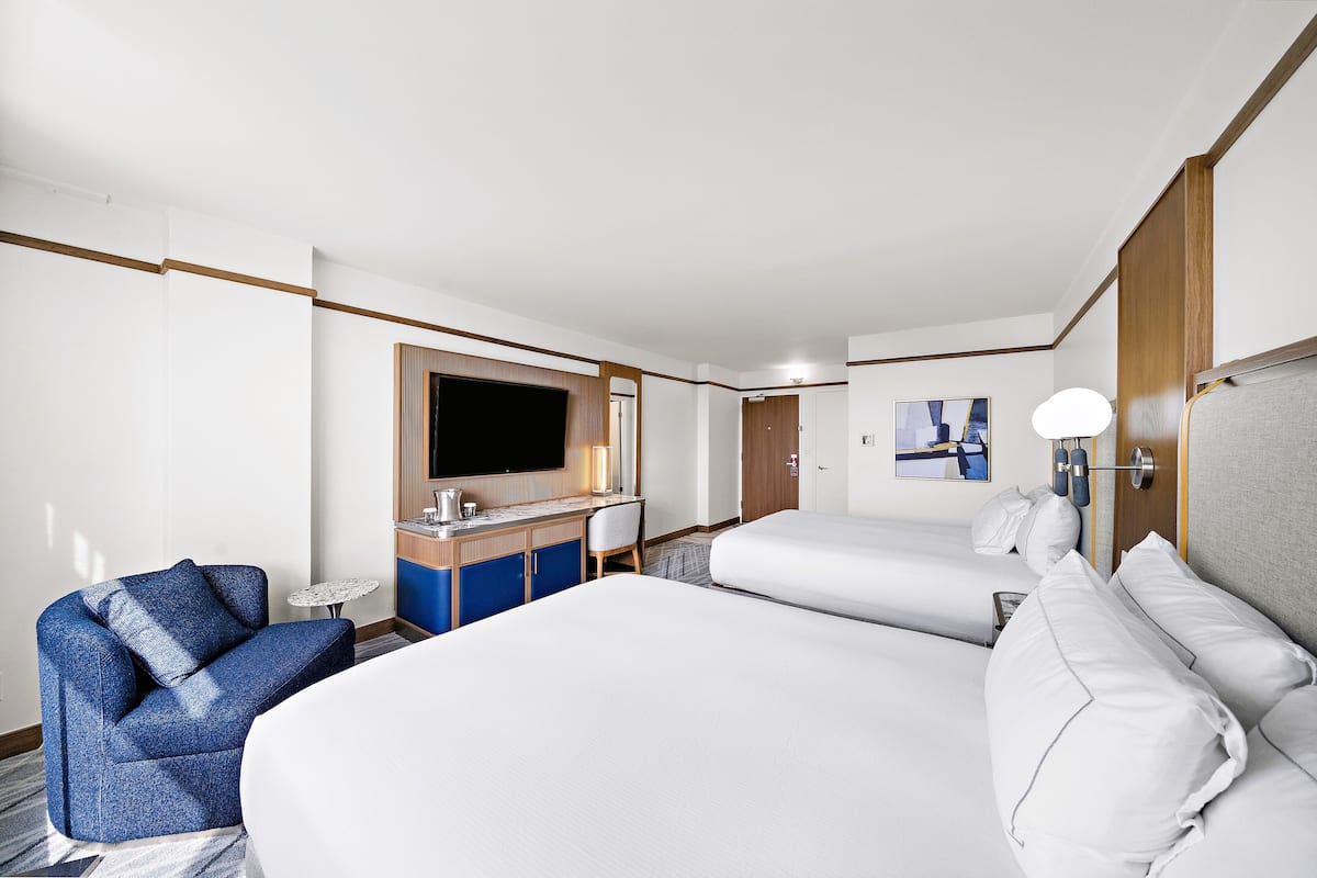 A hotel room with a large bed, a desk with a flat-screen TV, a chair, and a small table.