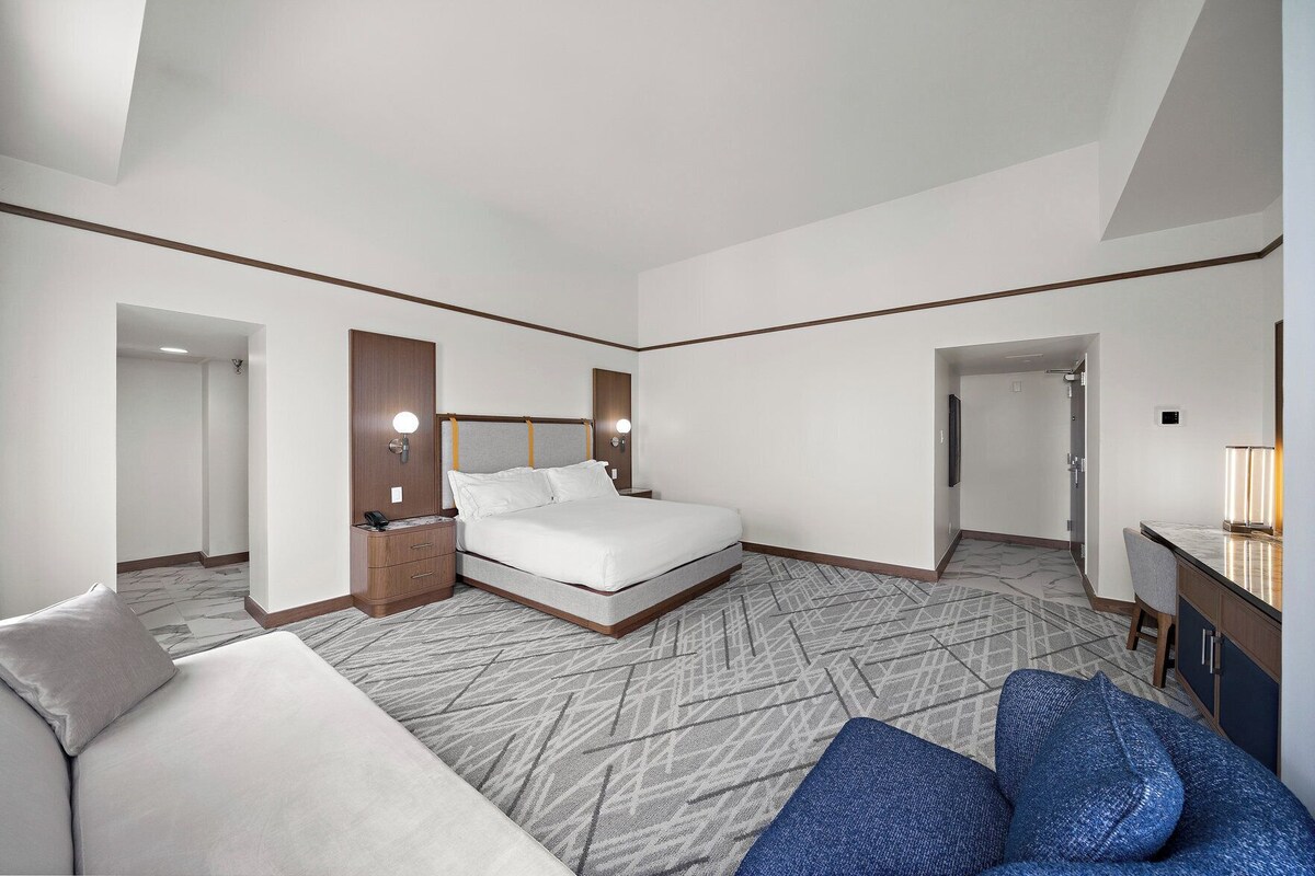 A hotel room with a bed, bedside tables, a desk, and a chair.