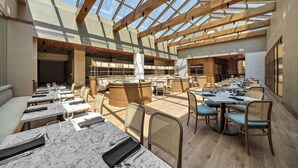 A spacious indoor area with multiple dining tables and chairs, a central bar area, and a high ceiling with skylights. - Hilton College Station & Conference Center (College Station)