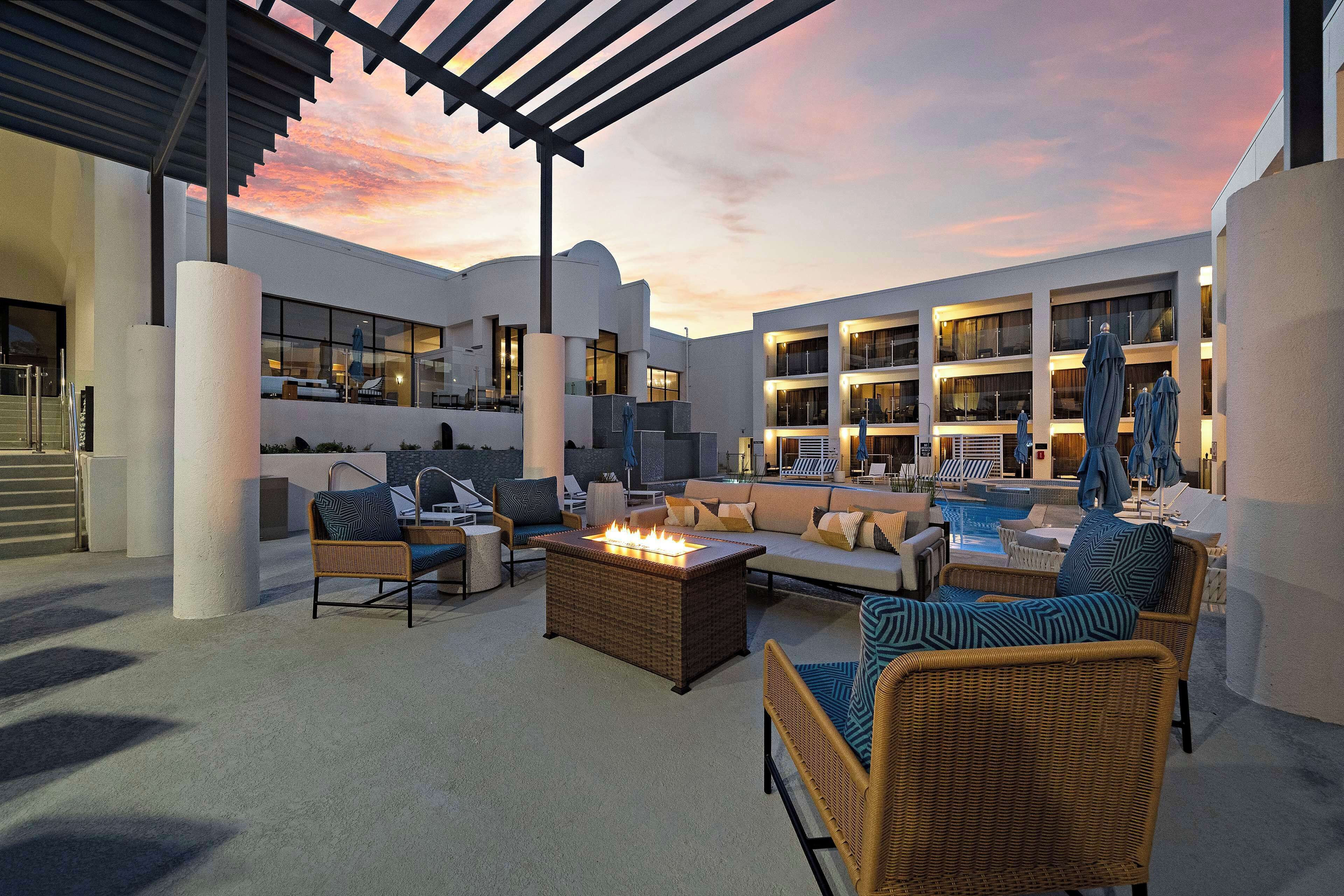 An outdoor lounge area with wicker furniture, a fire feature, and a pool.