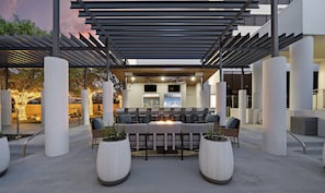 An outdoor seating area with a fire feature, surrounded by columns and a pergola.