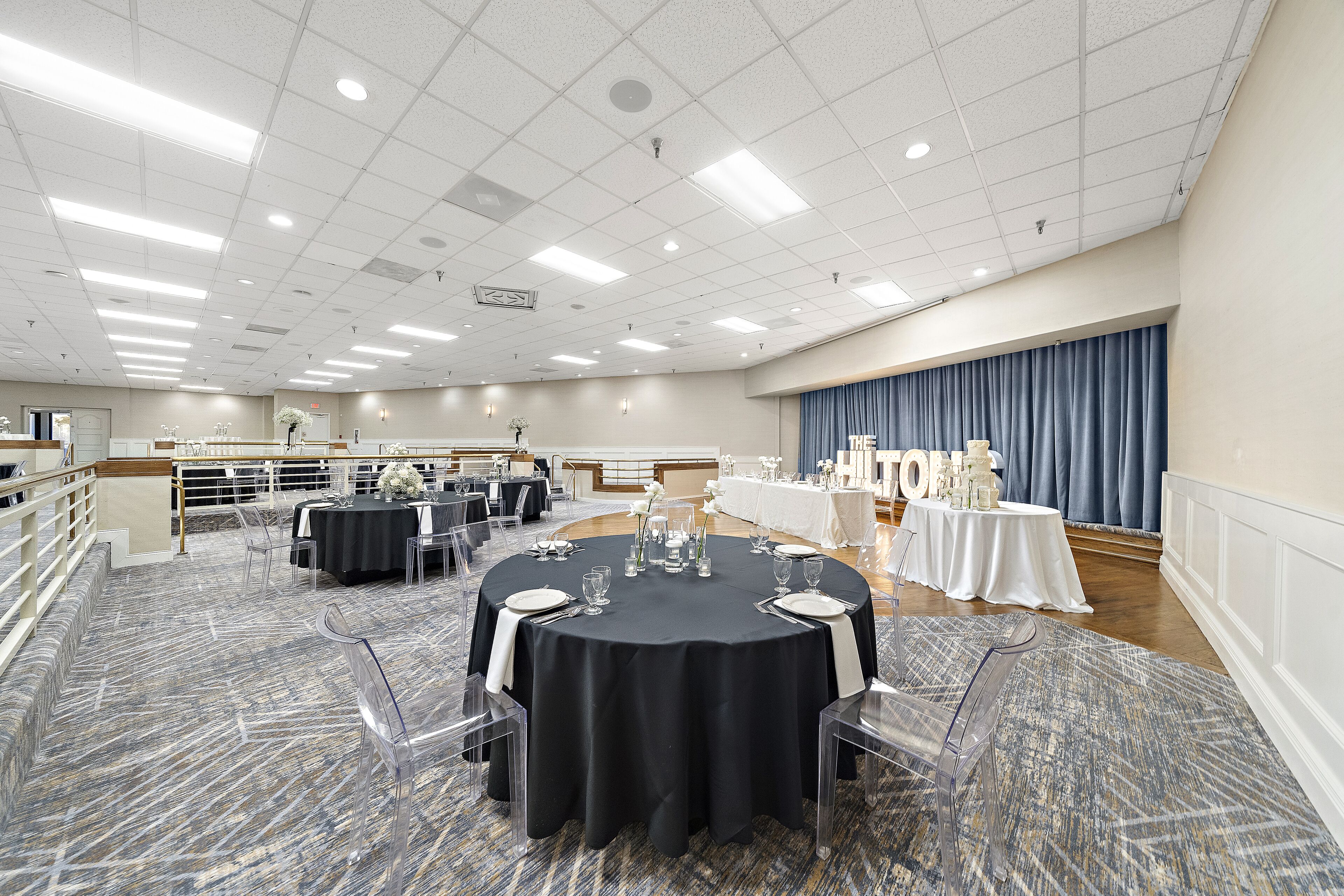 A conference room with round tables, clear chairs, and a stage area.