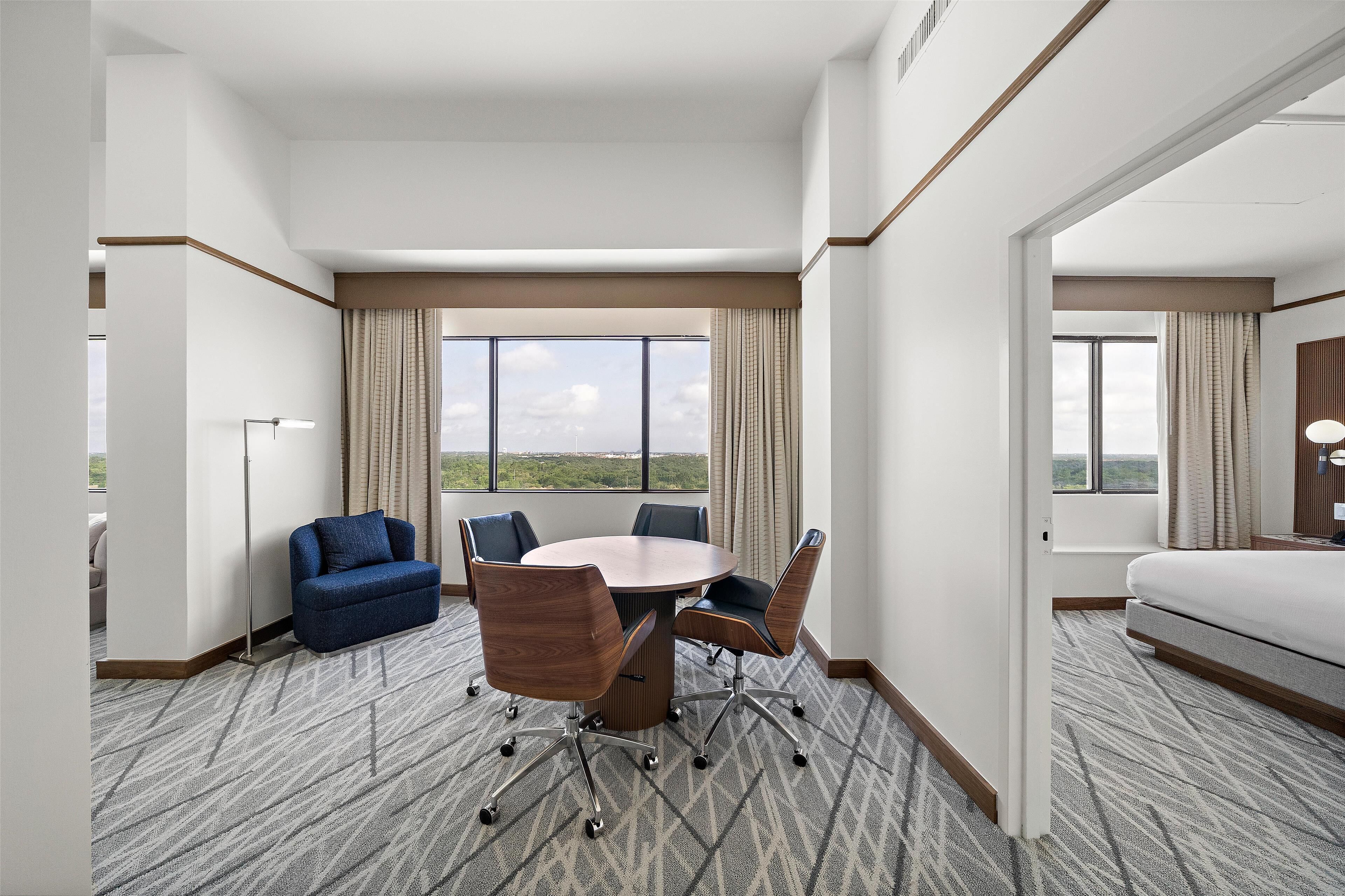 A hotel room with a large round table, four chairs, a sofa, and a bed.