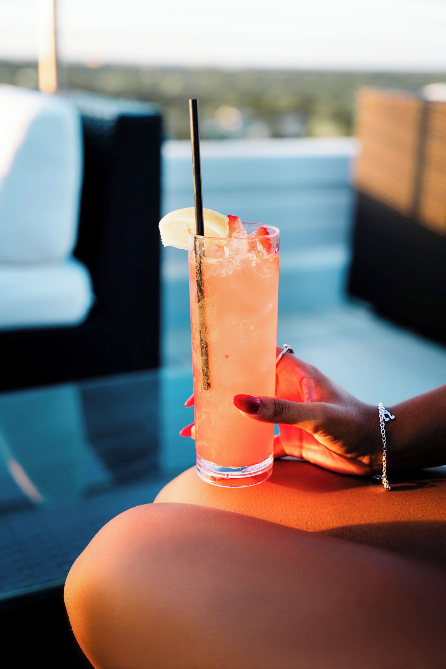A person holding a tall glass with a straw, resting on a table with a cushion.