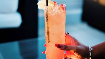 A person holding a tall glass with a straw, resting on a table with a cushion.