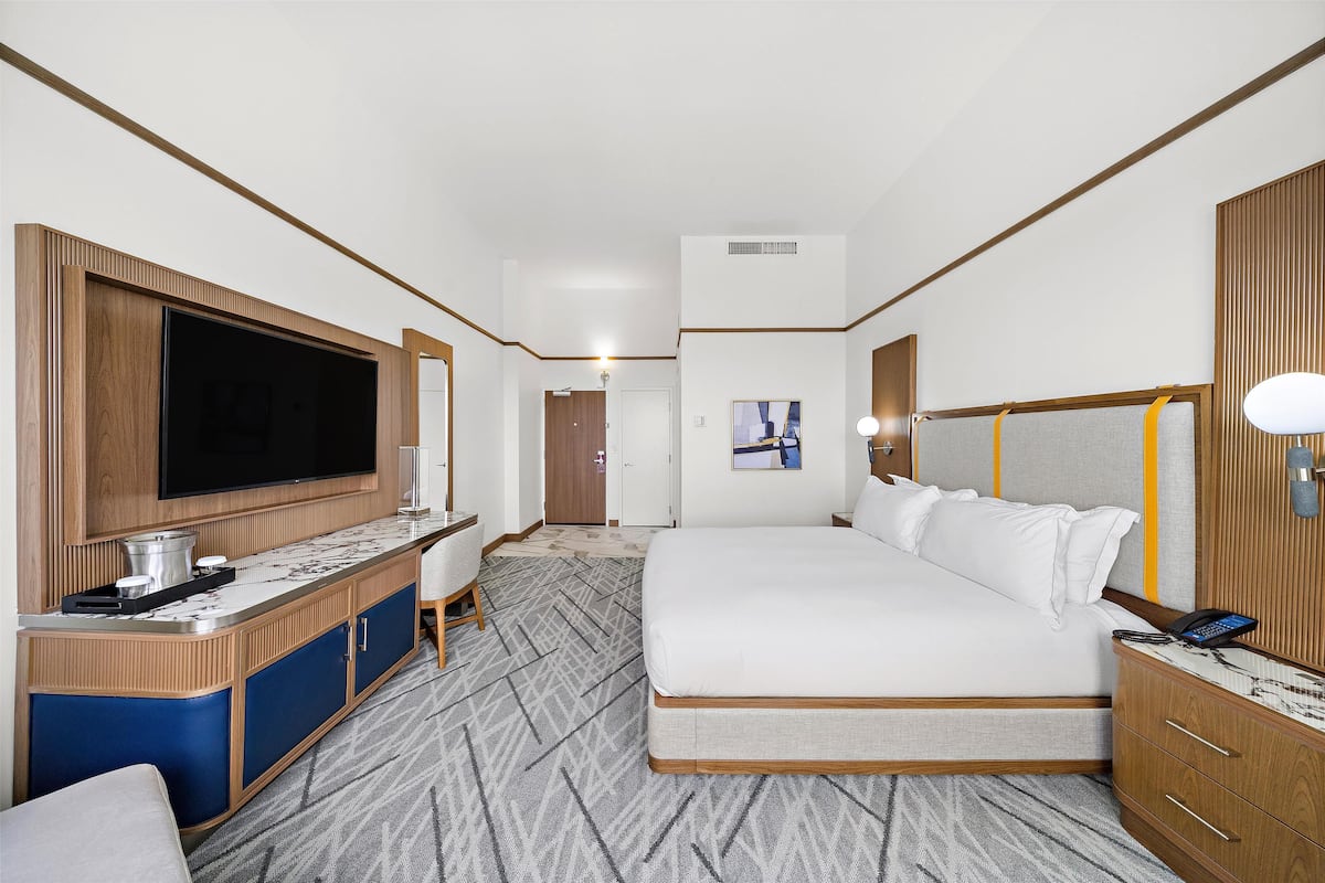 A hotel room with a large bed, a desk with a flat-screen TV, a minibar, and a wardrobe.