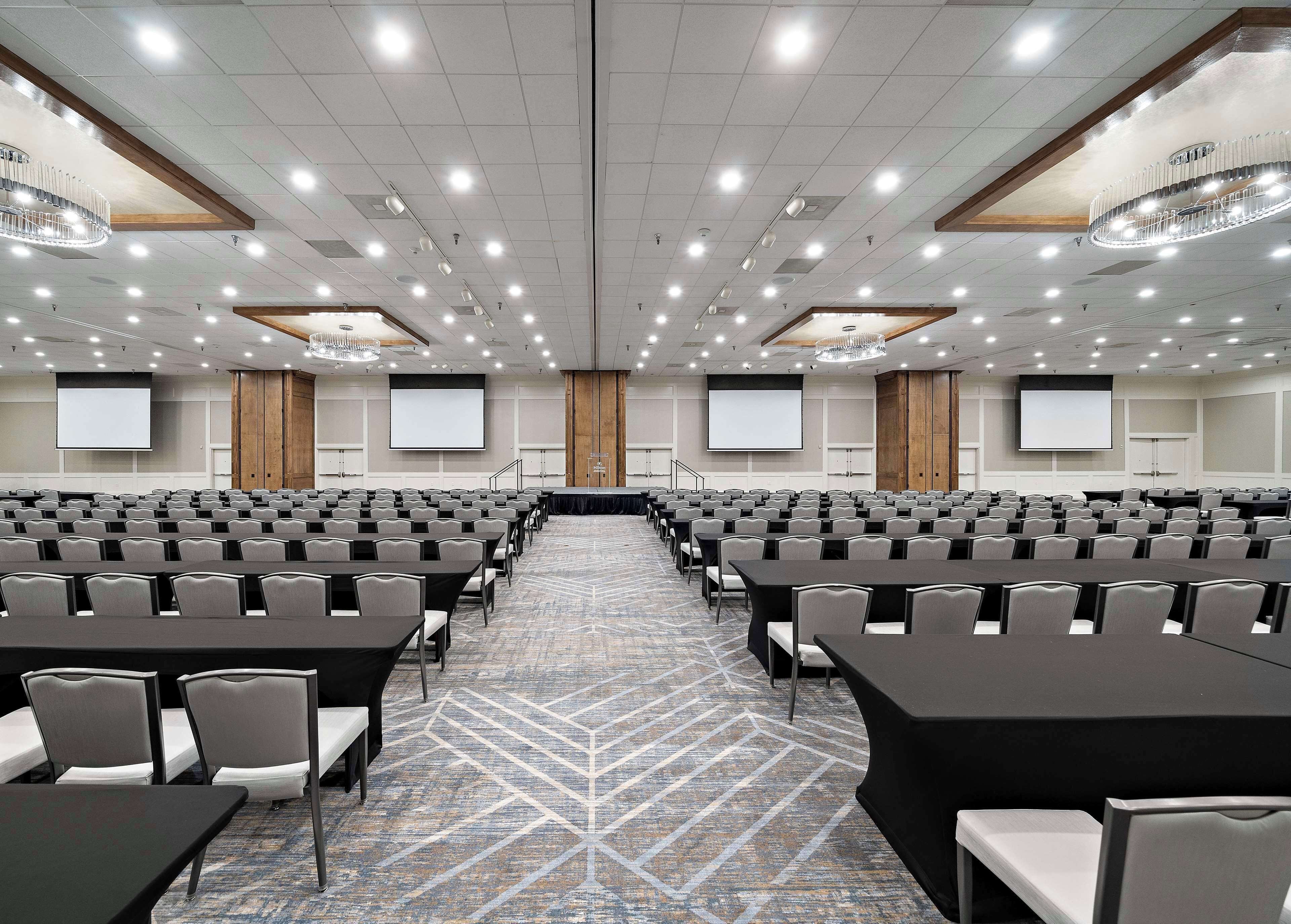 A conference room with rows of tables and chairs, a carpeted floor, and a large screen at the front.