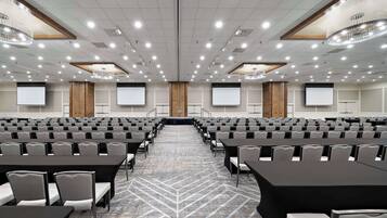 A conference room with rows of tables and chairs, a carpeted floor, and a large screen at the front.