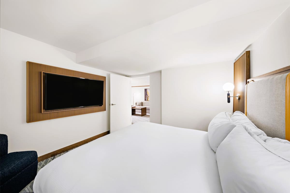 A hotel room with a large bed, a flat-screen TV mounted on the wall, a desk, and a chair.