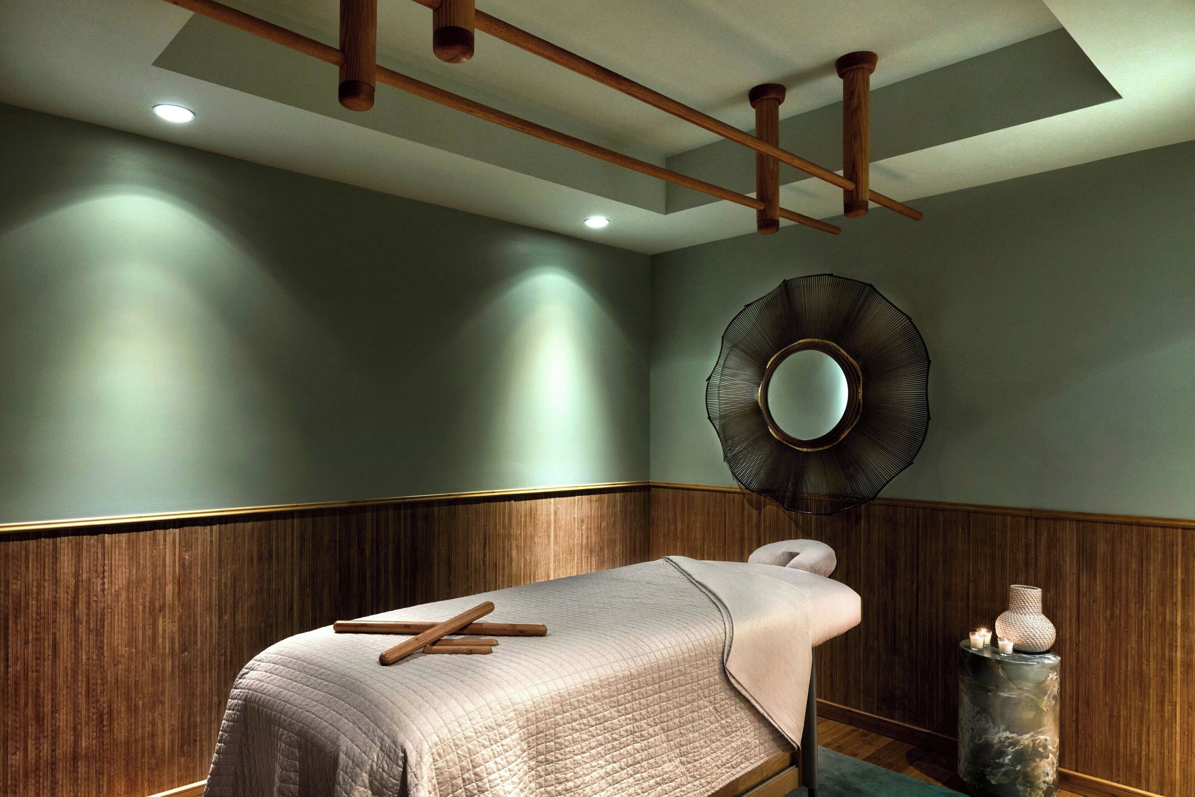 A room with a bed, wooden paneling, a round mirror, and a small table with candles.