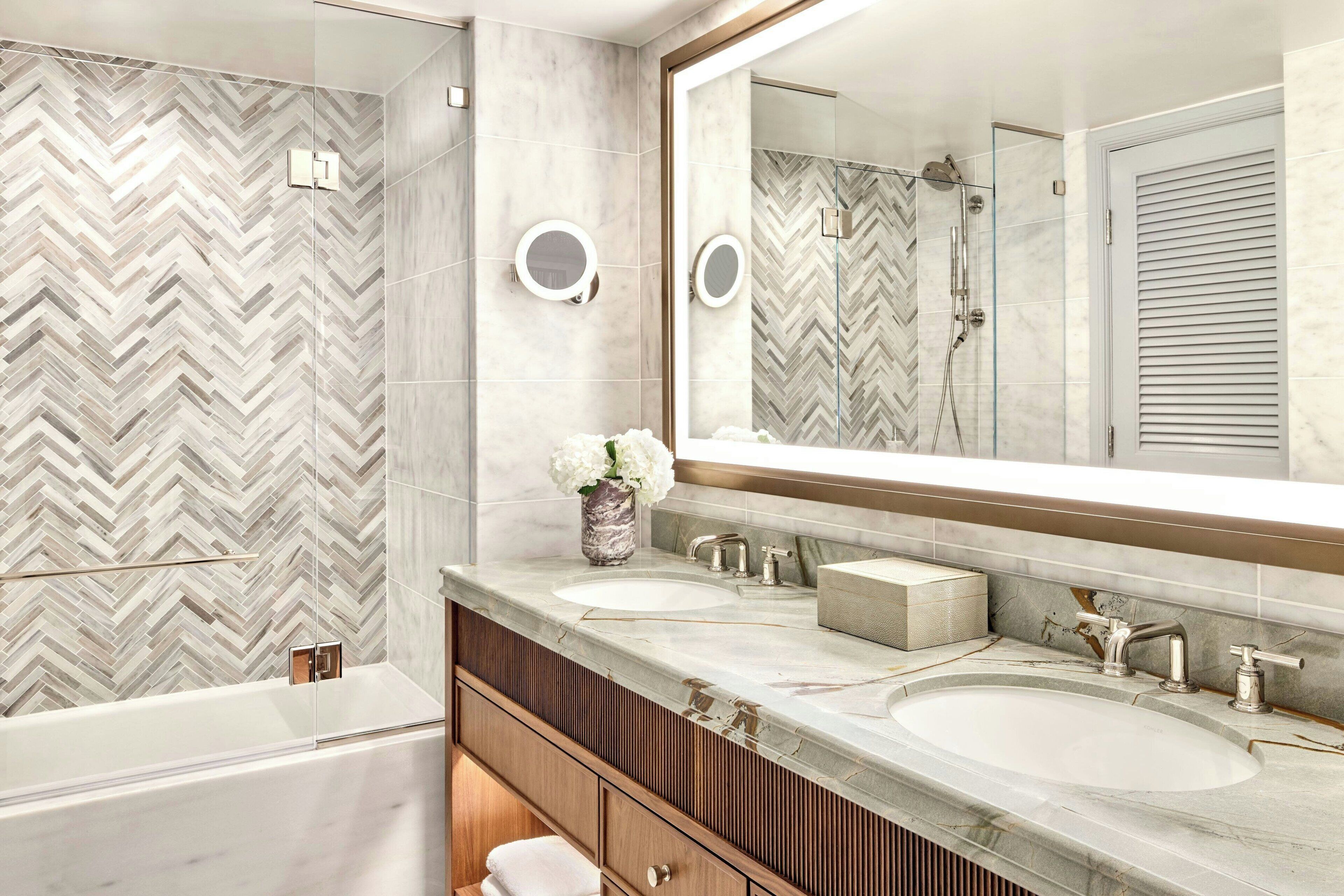 A modern bathroom with a large mirror, two sinks, and a shower.