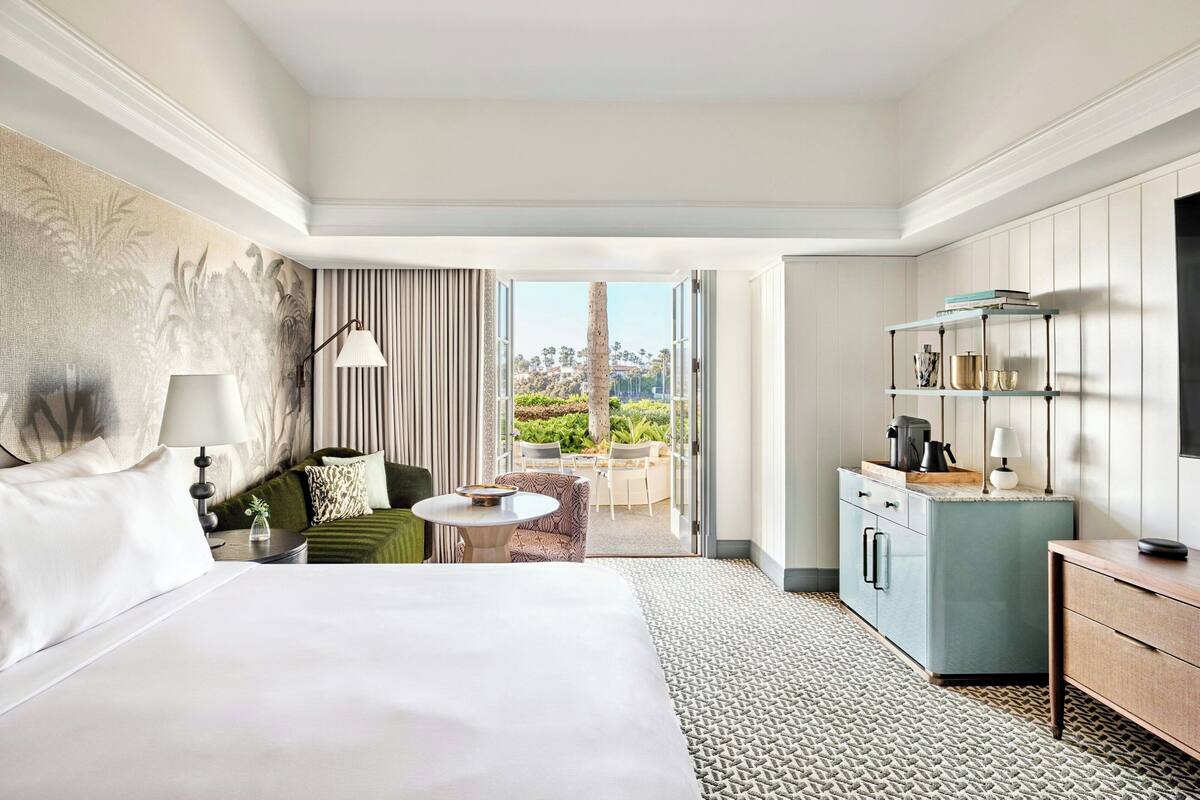 A hotel room with a large bed, a seating area with a table, a kitchenette, and a view of the outdoors.