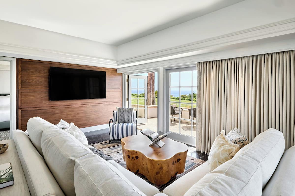 A modern living room with a large flat-screen TV mounted on a wooden panel, a white sofa, a striped armchair, and a wooden coffee table.